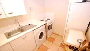 Une cuisine de taille réduite, équipée d’un évier, d’une cuisinière et d’un lave-linge.