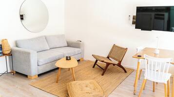 Una sala de estar moderna con un sofá gris, un espejo redondo, un televisor y una pequeña mesa de madera con sillas.
