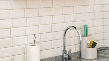 A kitchen with a granite countertop, a stainless steel sink, a faucet, a shelf with glassware, and a roll of paper towels.