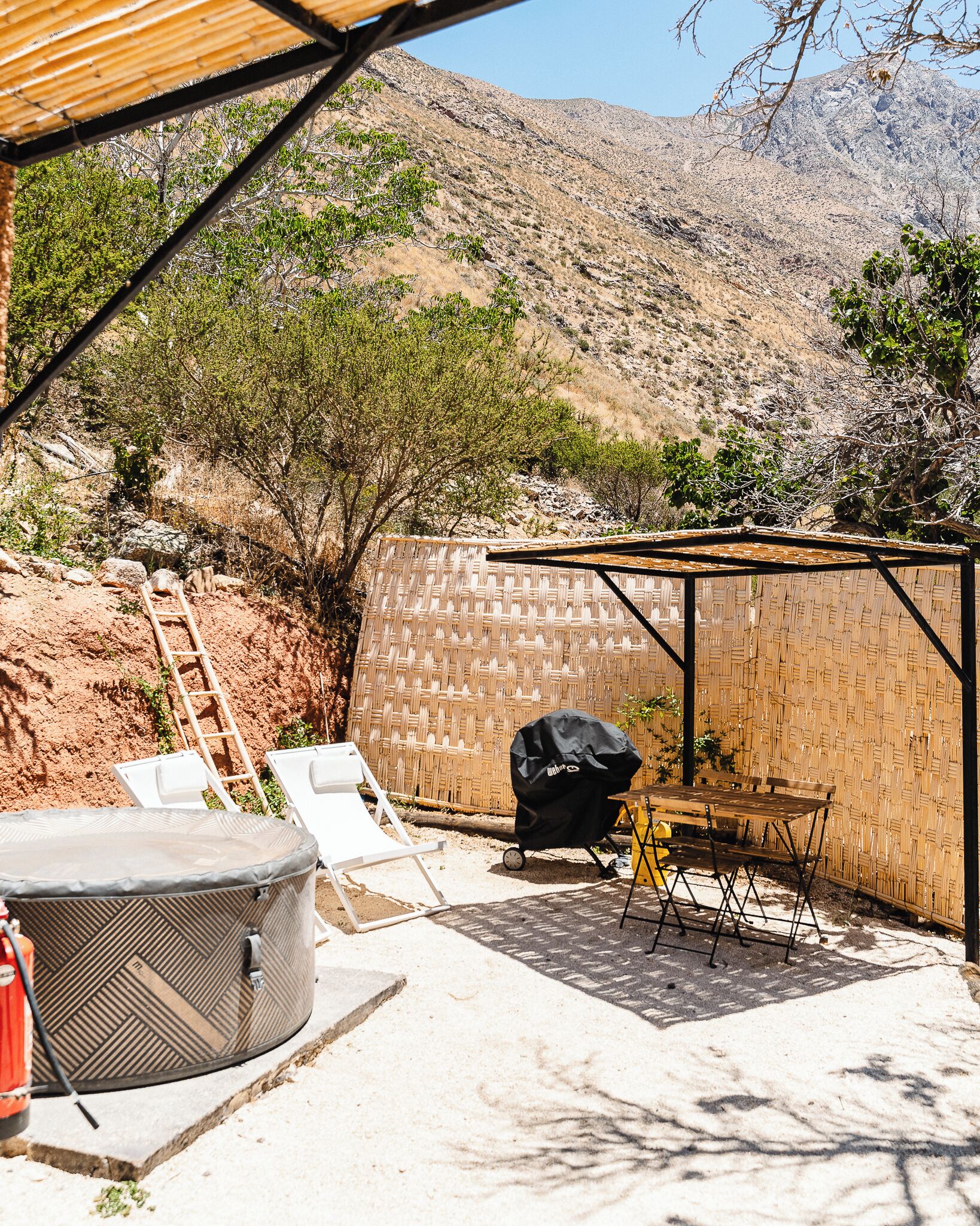 A backyard with a hot tub, lounge chairs, a barbecue grill, and a wooden table.