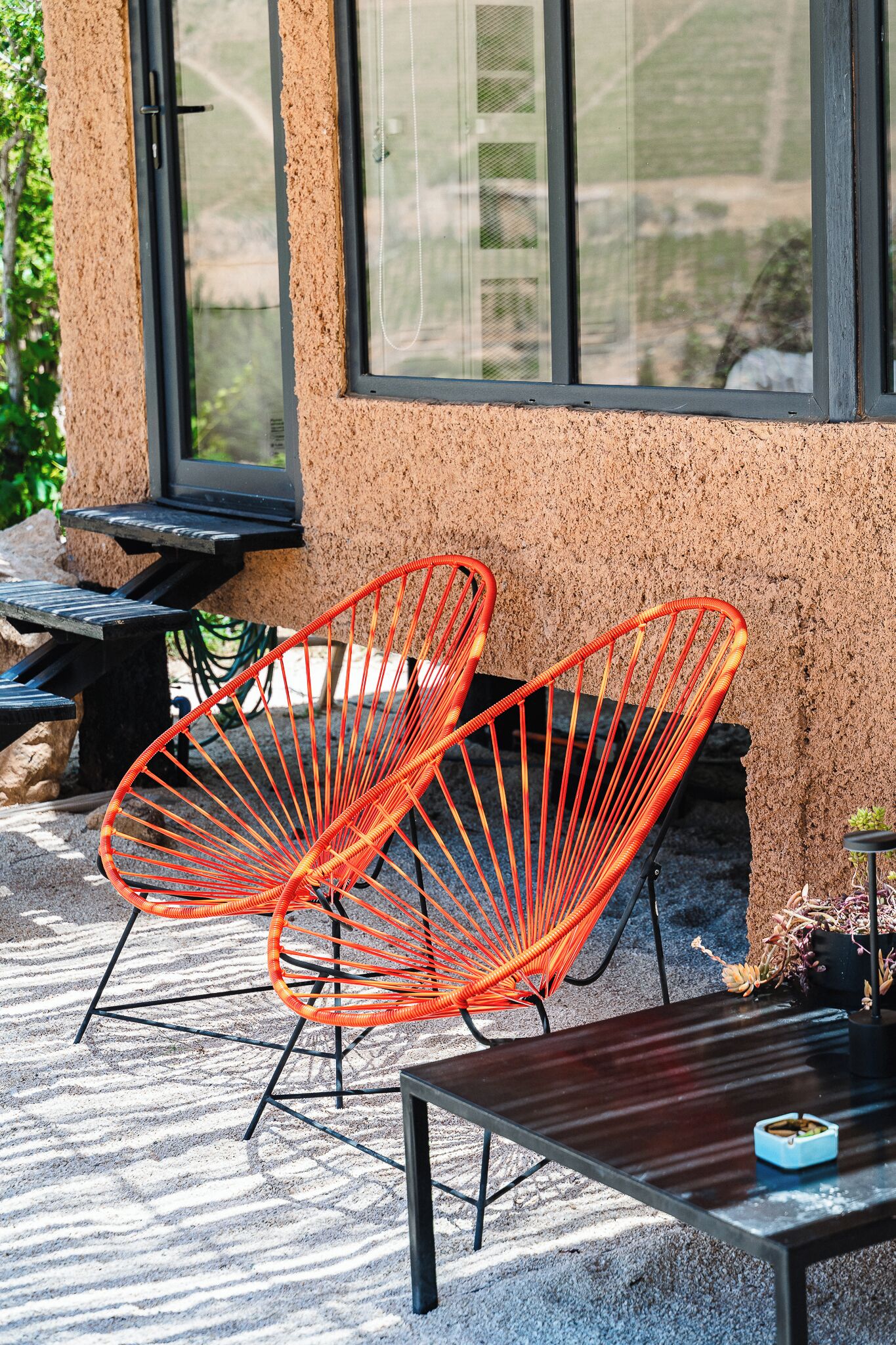 A patio area with two orange wire chairs, a wooden table, and a small blue bowl.