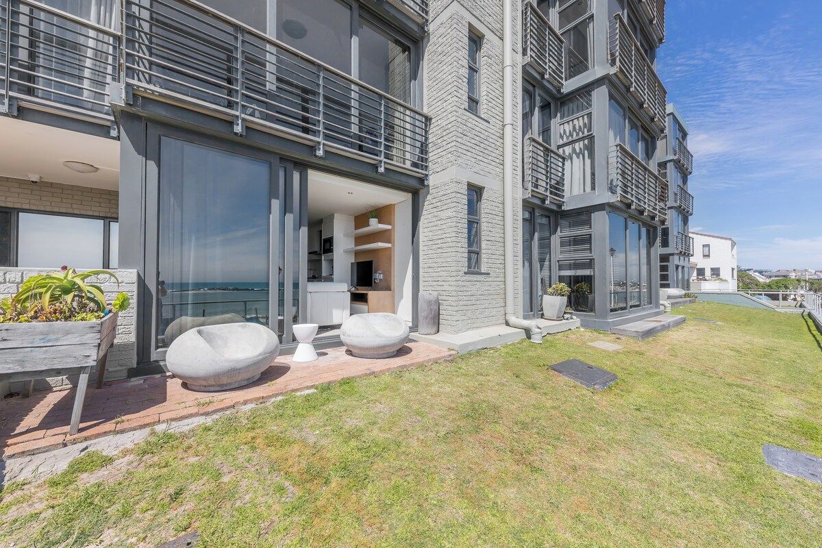 A modern multi-story building with a balcony, large windows, and a well-maintained lawn.