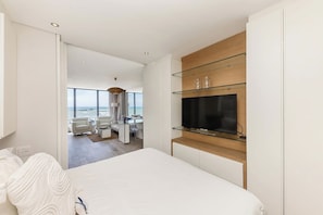 Ein modernes Hotelzimmer mit einem großen Bett, einem Fernseher auf einem Holzboden und Blick aufs Meer.