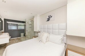 A modern bedroom with a large bed, a glass shower enclosure, and a white headboard.
