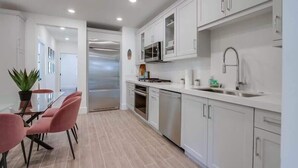 Una cocina moderna con armarios blancos, electrodomésticos de acero inoxidable y un comedor con sillas rosadas.