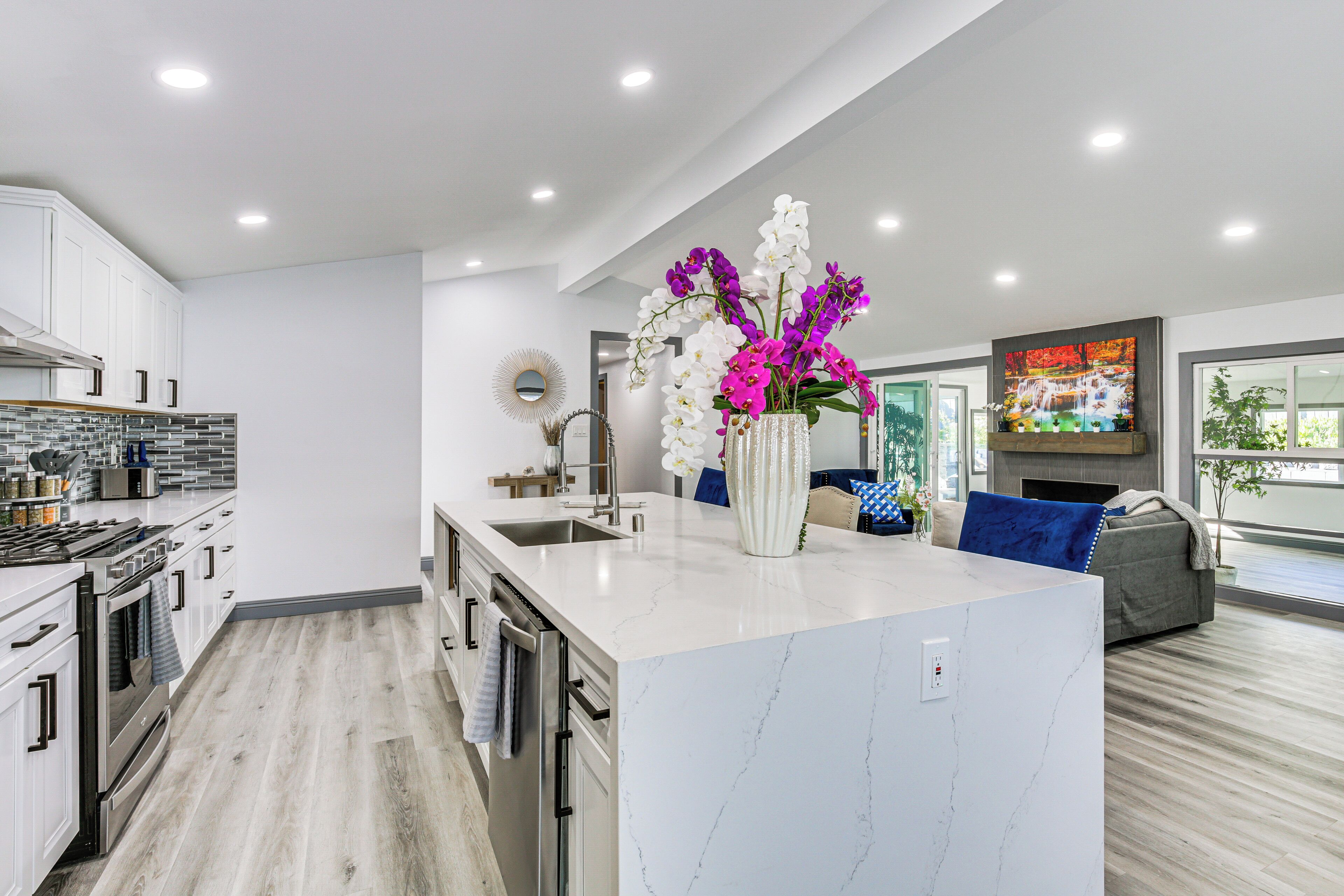 A modern kitchen with white cabinets, a marble island, and a vase of flowers.