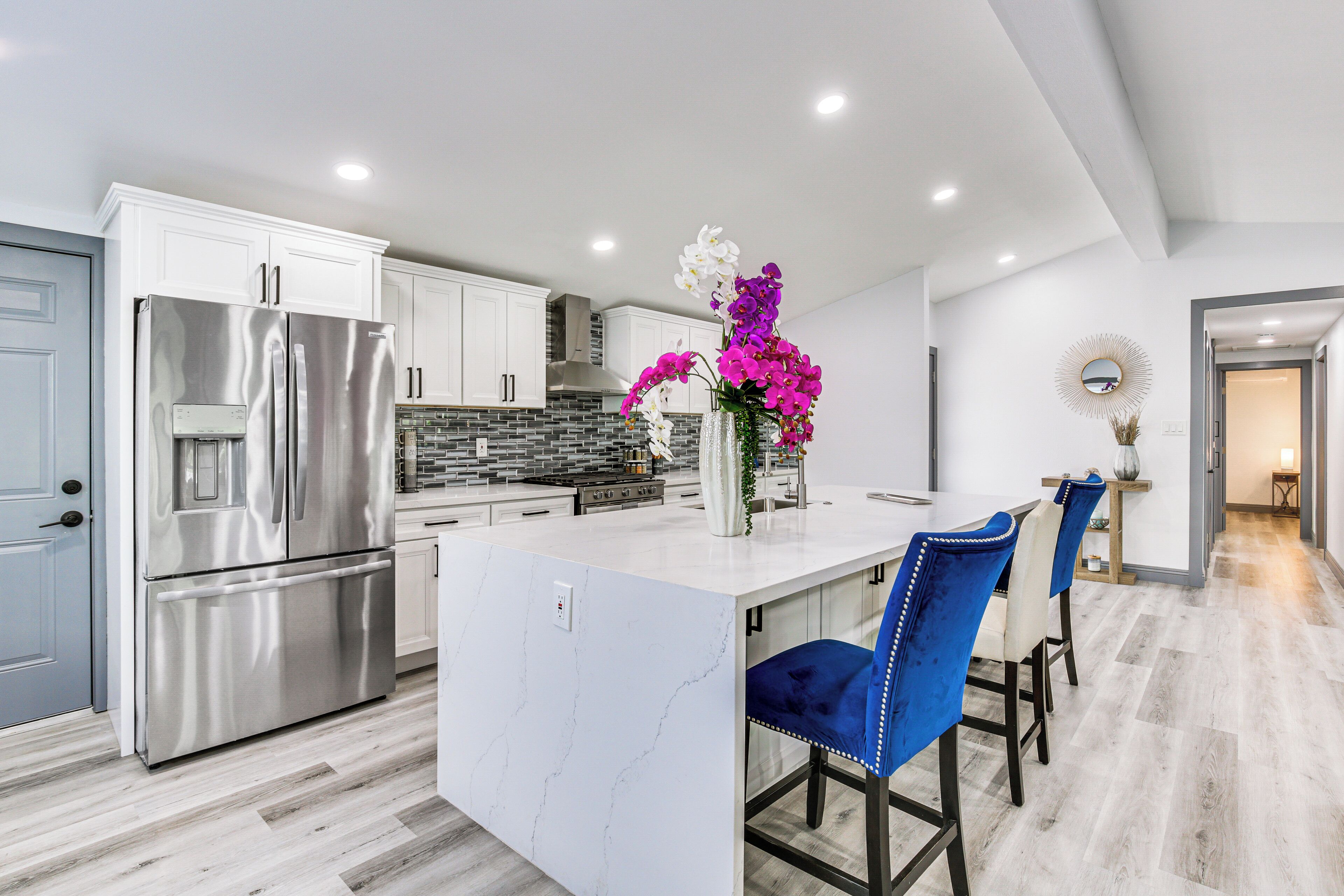 A modern kitchen with white cabinets, a stainless steel refrigerator, and a marble island.