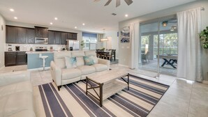 A spacious living area with a sofa, coffee table, and a striped rug. There is a kitchen with dark cabinets and a ceiling fan. A sliding glass door leads to an outdoor patio. - 14 Mi to Wdw: Family-friendly Home w/ Movie Room! (Kissimmee)