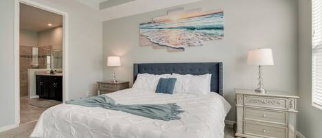 Un dormitorio con una cama grande, una mesita de noche, una lámpara de pared y un cuadro de una playa.