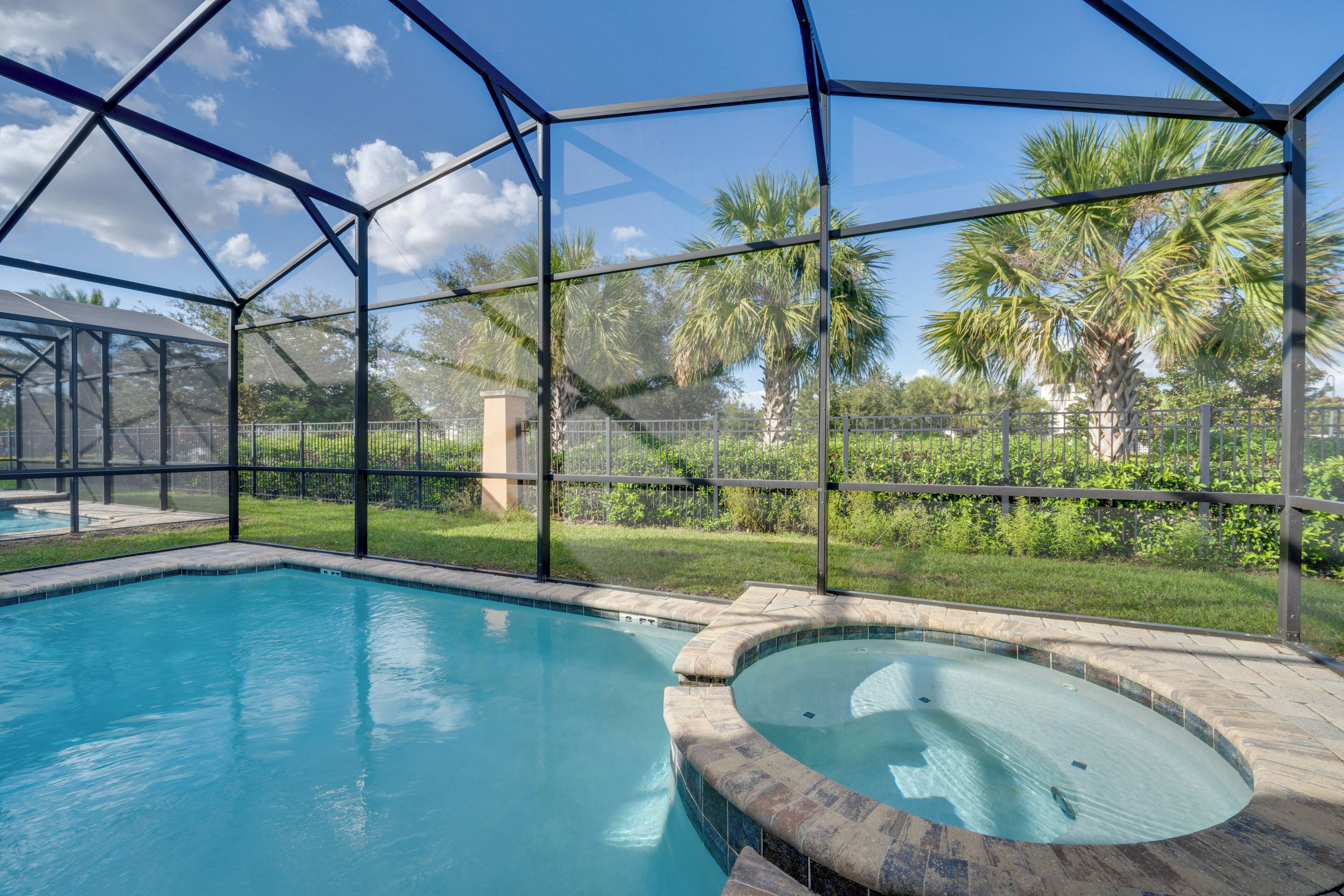 A swimming pool with a hot tub, surrounded by a glass enclosure, and views of palm trees and greenery.