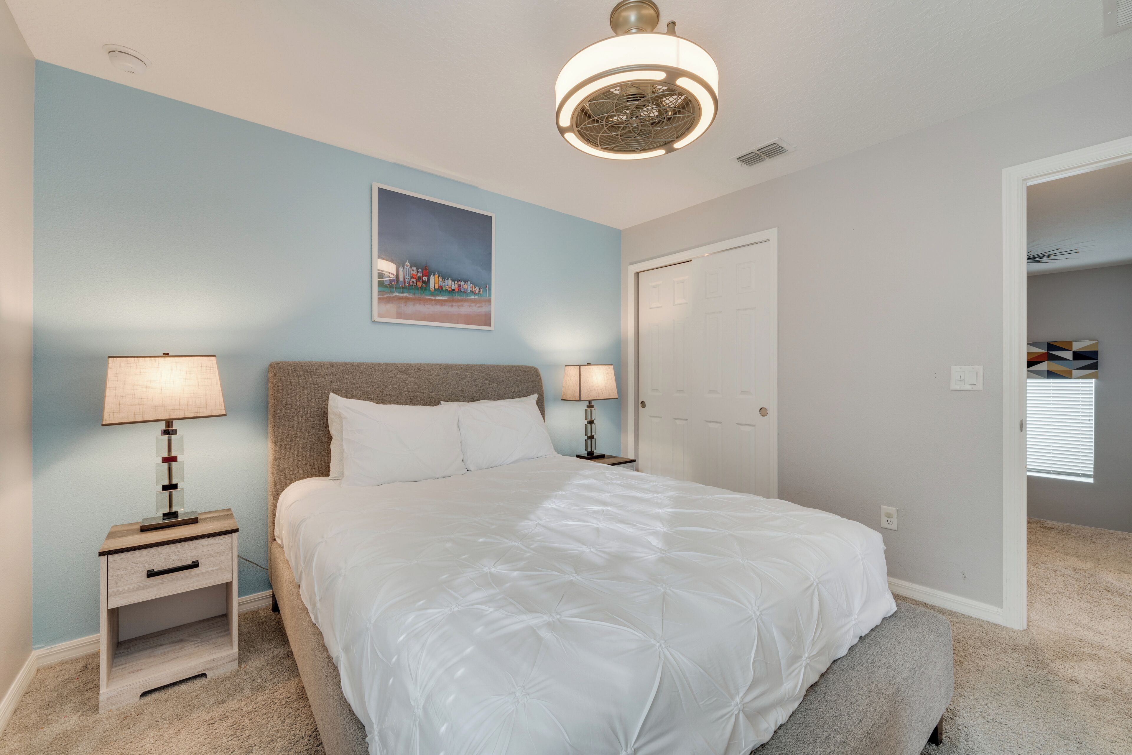 Une chambre à coucher avec un grand lit, deux tables de chevet avec des lampes, une porte et un tableau au mur.