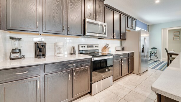A modern kitchen with dark wood cabinets, stainless steel appliances, and a white countertop. - 14 Mi to Wdw: Family-friendly Home w/ Movie Room! (Kissimmee)