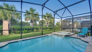 A swimming pool with a hot tub, surrounded by a glass enclosure, palm trees, and a chair. - 14 Mi to Wdw: Family-friendly Home w/ Movie Room! (Kissimmee)