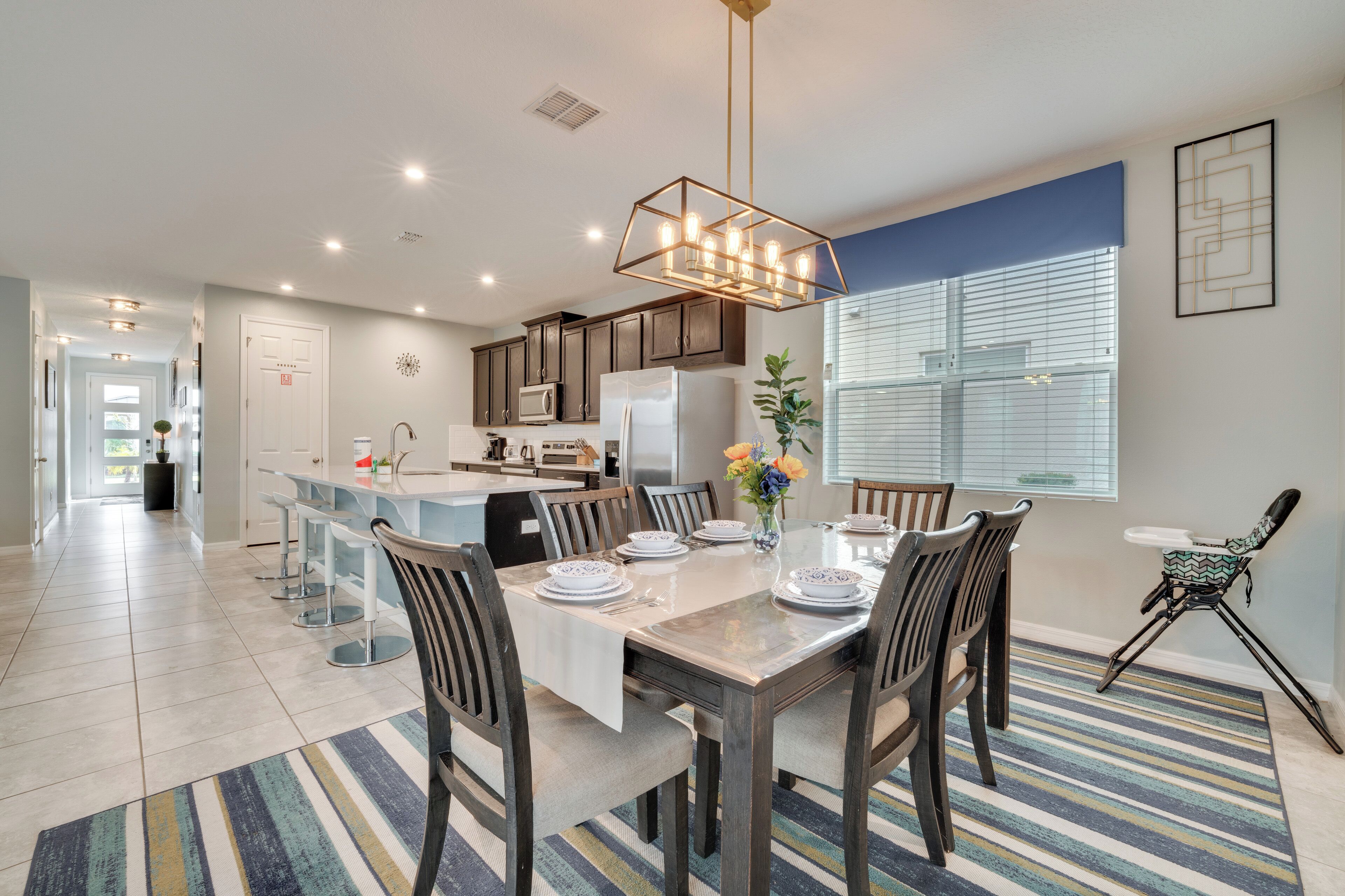 A modern kitchen with a central island, stainless steel appliances, and a dining area with a striped rug.