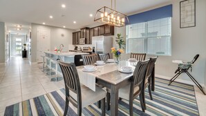 A modern kitchen with a central island, stainless steel appliances, and a dining area with a striped rug. - 14 Mi to Wdw: Family-friendly Home w/ Movie Room! (Kissimmee)