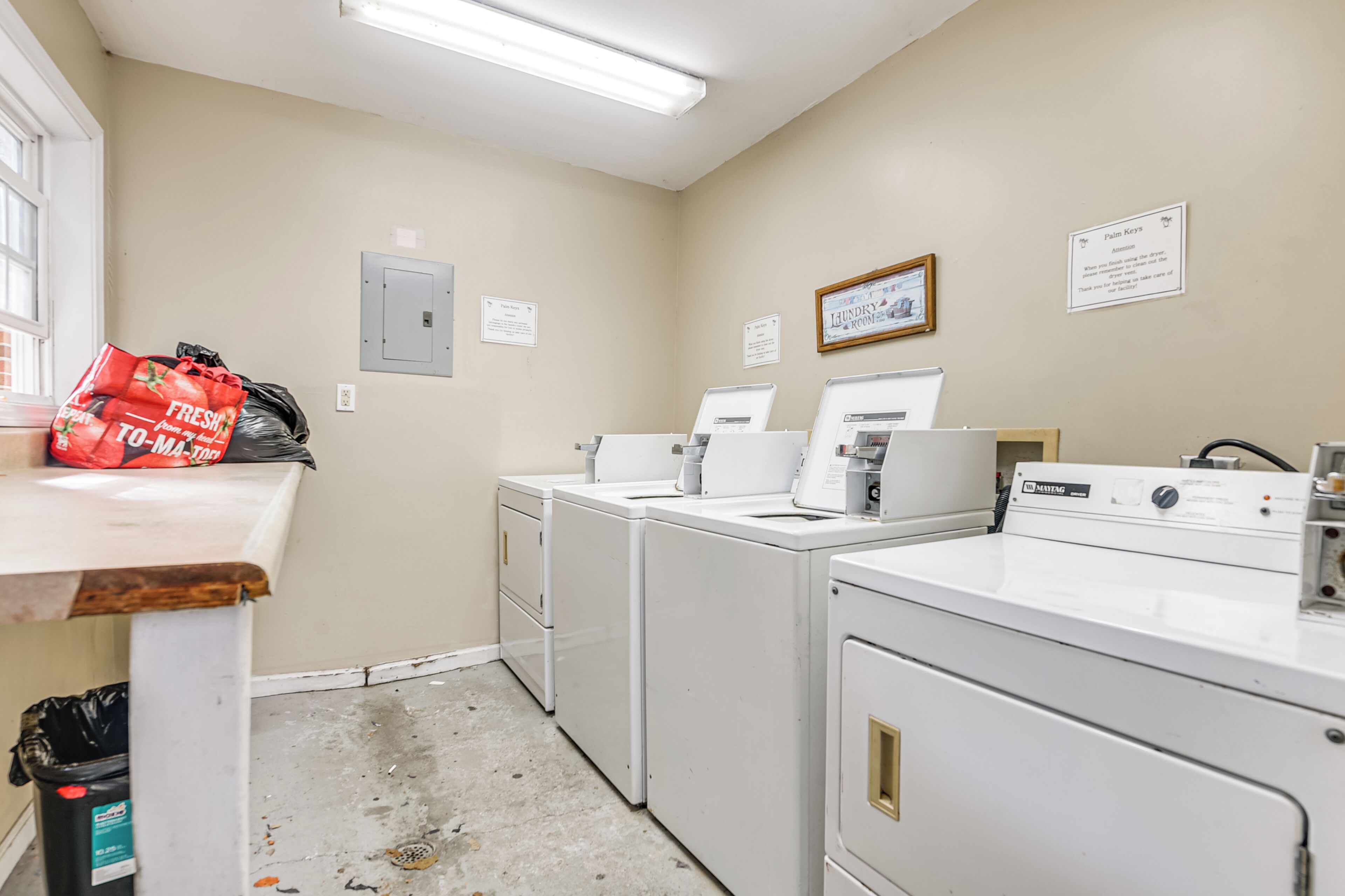 A laundry room with four white washers and dryers, a trash bin, and a red bag on a counter.