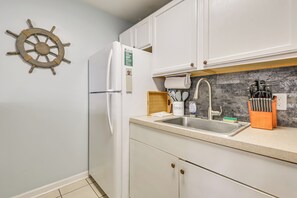 Une cuisine avec des meubles blancs, un évier en acier inoxydable, une décoration en forme de roue de navire en bois et un bloc à couteaux.