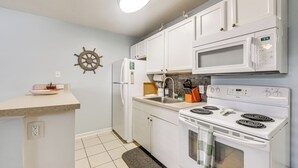 Una cucina con mobili bianchi, un forno a microonde, un piano cottura, un lavandino e una decorazione a forma di timone di nave.