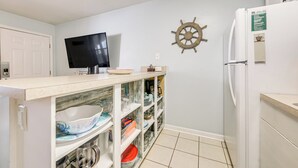 Una cucina compatta con TV integrata, decorazione a forma di timone da nave e frigorifero con insegna verde.