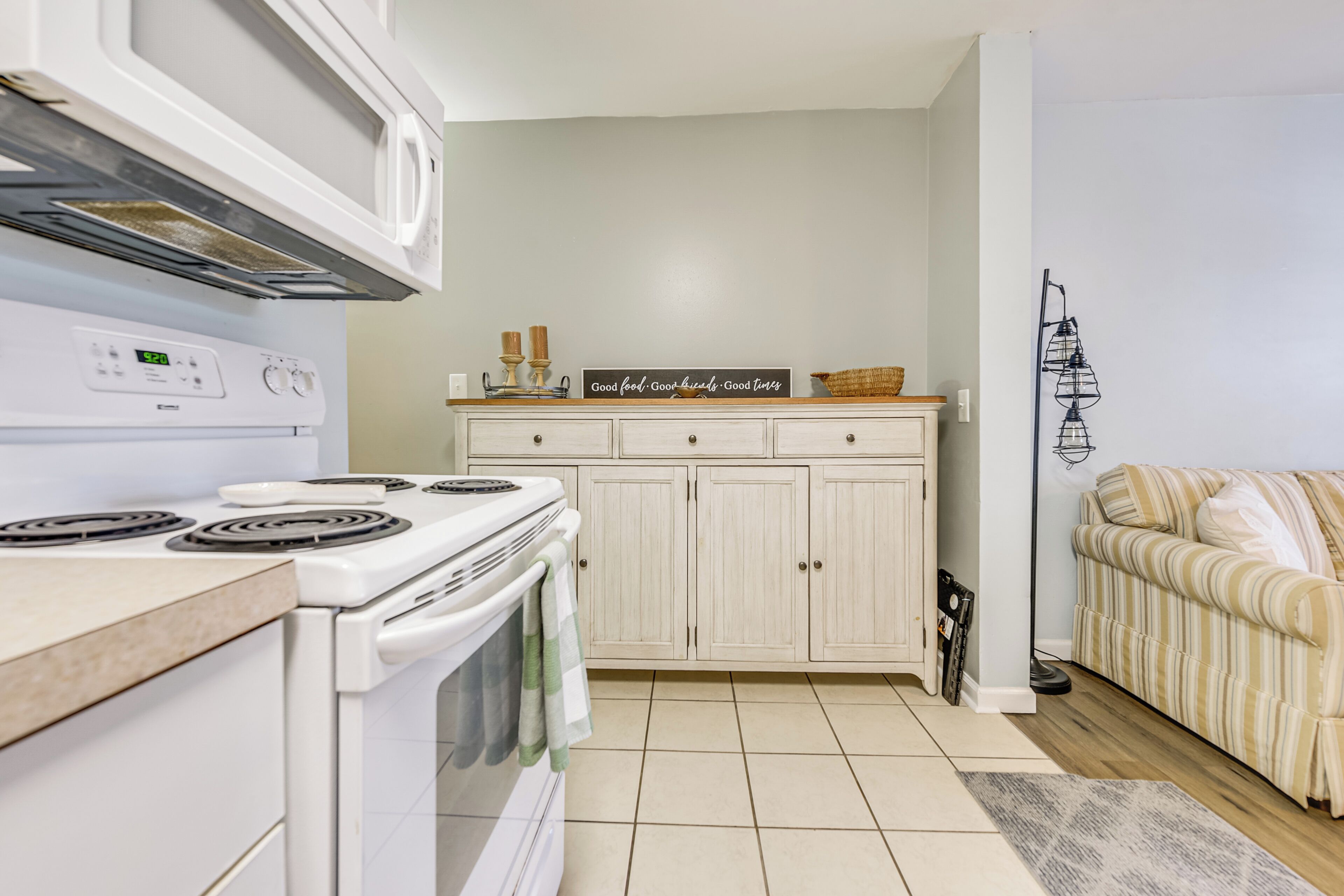 A kitchen with white cabinets, a stove, and a microwave. There is a sign on the counter that says "Good food. Good friends. Good time."
