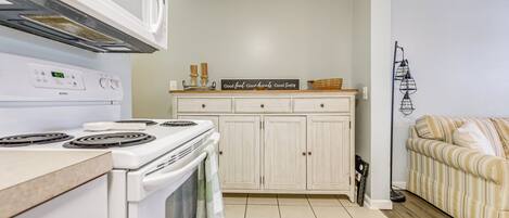 A kitchen with white cabinets, a stove, and a microwave. There is a sign on the counter that says "Good food. Good friends. Good time."