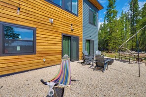 Une maison moderne à deux étages, construite en bois, dotée d’une terrasse en gravier, de meubles d’extérieur et d’un hamac.