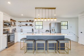 Une cuisine moderne avec des meubles blancs, un îlot central doté de tabourets, un four encastré et un luminaire suspendu.