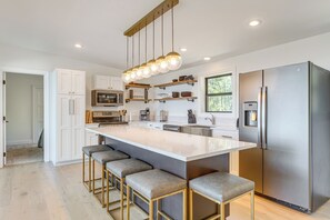 Una cocina moderna con una isla grande, taburetes de bar, electrodomésticos de acero inoxidable e iluminación colgante.