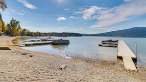 A lakeside dock with boats, a sandy beach, and a forested shoreline.