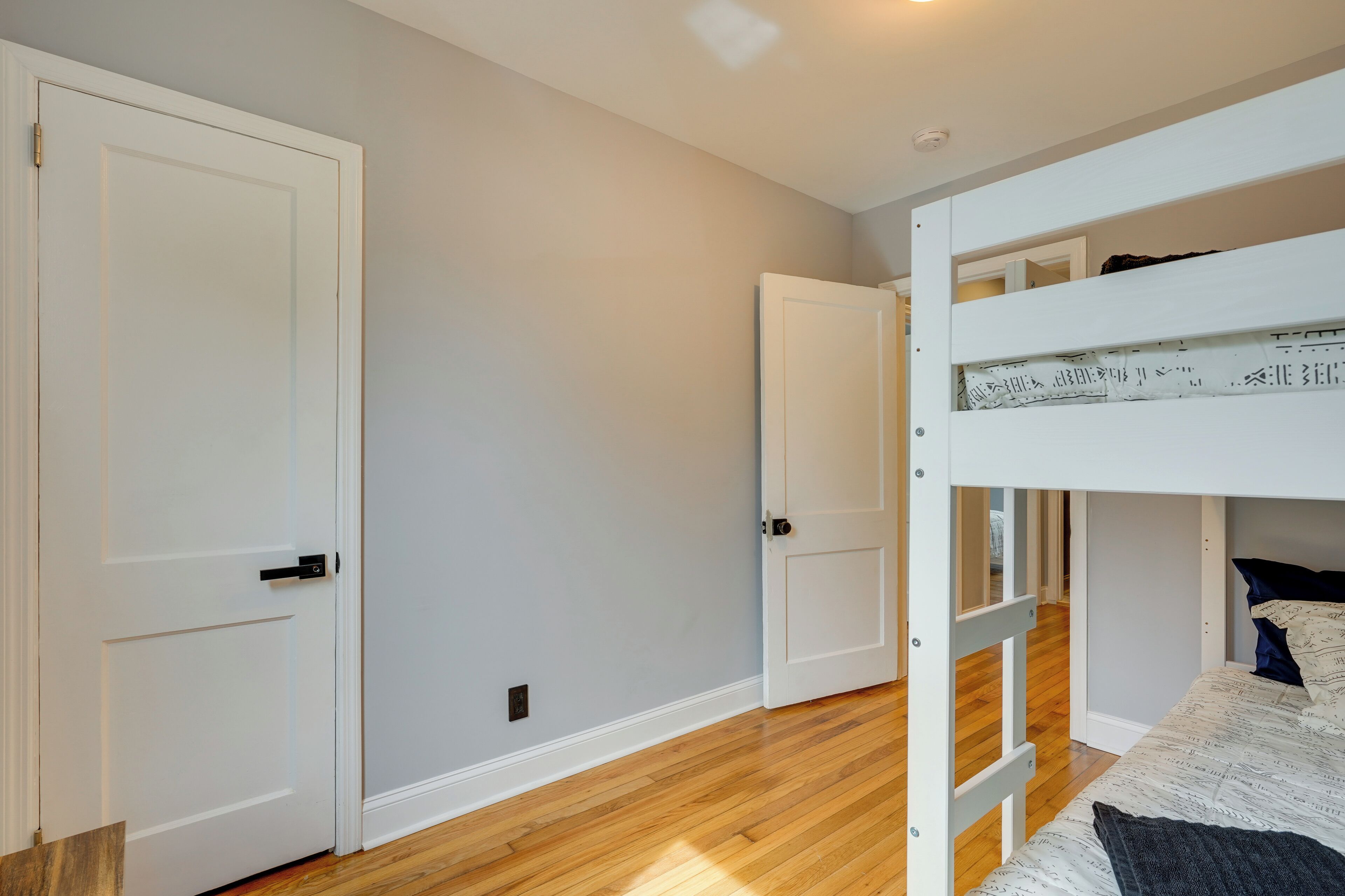 A bedroom with a bunk bed, wooden flooring, and white walls.
