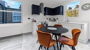 Une cuisine moderne avec des meubles blancs, une table à manger noire et des chaises orange.