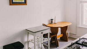 Une cuisine équipée d’une cuisinière, d’une table en bois, d’une poubelle et d’une horloge murale.