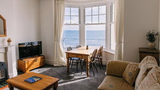 Un salon doté d’une baie vitrée donnant sur la mer, d’une table basse en bois, d’un canapé et d’un téléviseur.