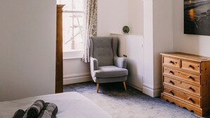 Une chambre à coucher avec un lit, une chaise, une commode en bois et un tableau accroché au mur.