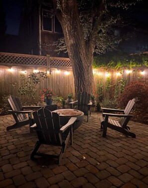 Un patio exterior con sillas Adirondack, una mesa redonda y un árbol.