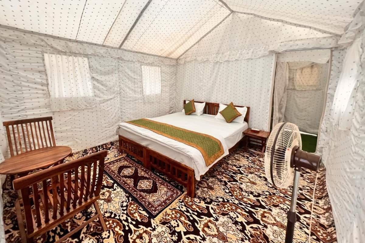 A tent-style room with a bed, wooden furniture, a fan, and patterned rugs.