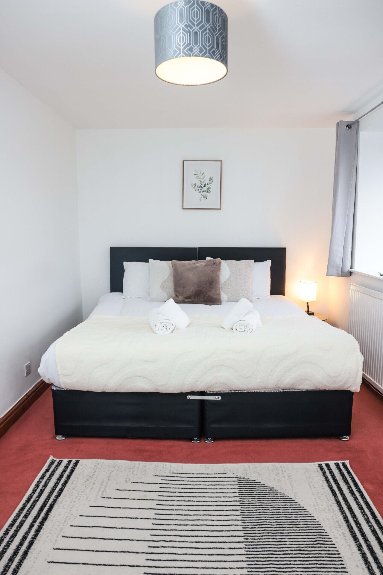 Una cama bien hecha con sábanas blancas, cabecera oscura e impresión enmarcadas de motivos botánicos en la pared.