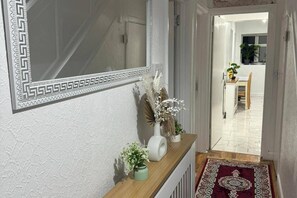 Ein Flur mit einem dekorativen Spiegel, einem Holzkonsolentisch mit Vasen und einem gemusterten Teppich, der zu einem Essbereich führt.