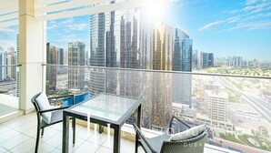 A balcony with a glass table and wicker chairs, overlooking a cityscape with modern skyscrapers. - LUX  The Bonnington JLT Suite 2 (Dubai)