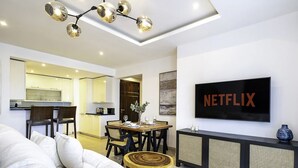 A modern living room with a flat-screen TV, a dining area, and a kitchen in the background. - LUX  The Bonnington JLT Suite 2 (Dubai)