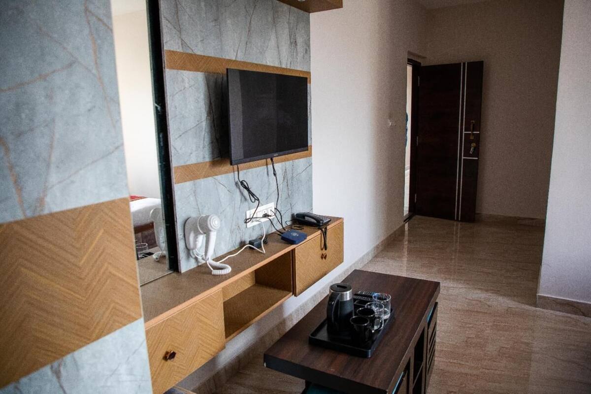 Moderni hotellihuone, jossa on marmoriseinä, seinälle asennettu televisio, puinen konsolipöytä, jossa on puhelin, sekä tarjoilupöytä, jossa on kuppeja ja kahvipannu.