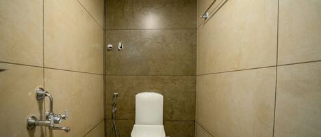 Un baño pequeño con azulejos, un inodoro, ducha de mano y un ventilador fijado a la pared.