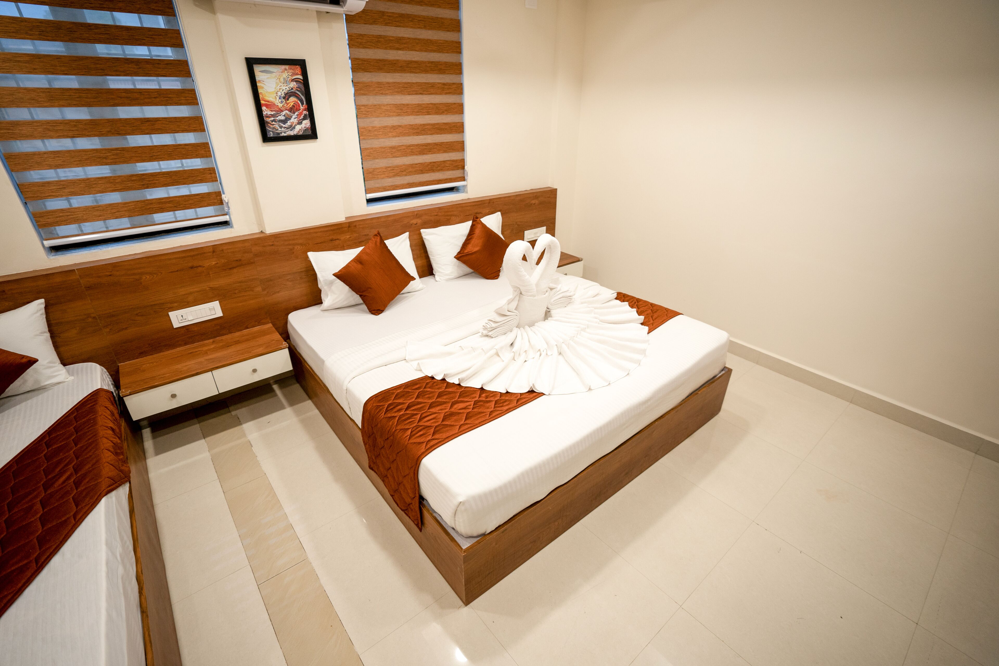 A modern hotel room with a large bed, wooden headboard, and a view of the city through large windows.