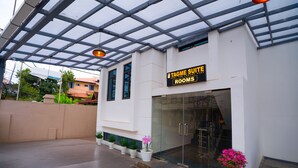 Een hotel ingang met een glazen deur, een bord met 'Tagme Suite Rooms' en plantenbakken voor de deur.