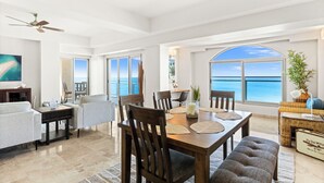A spacious living area with a dining table, chairs, and a large window offering a view of the ocean. - Charming 2-bedroom corner deluxe condo in Cupecoy with ocean and sunset view  (Cupecoy, St. Maarten)