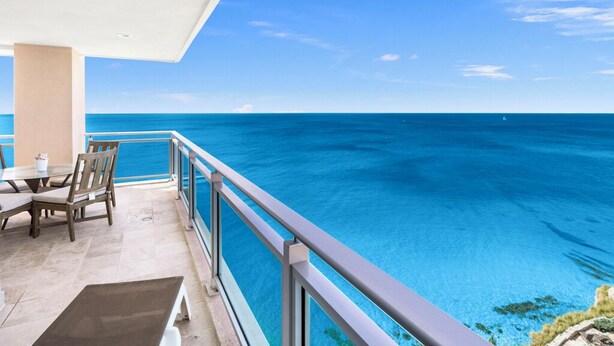 A balcony with a view of the ocean, a table with chairs, and a railing. - Charming 2-bedroom corner deluxe condo in Cupecoy with ocean and sunset view  (Cupecoy, St. Maarten)