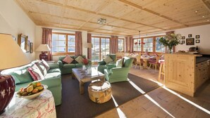 Un vaste salon doté d’un plafond en bois, de canapés verts, d’une table basse et d’un coin repas avec un buffet et une table en bois.