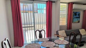 A dining area with a glass table, four chairs, and a view of a building through a sliding door. - Ginger House. Charming 3-bedroom townhome, fast WiFi, A/C in enchanting Rincón (Rincón)