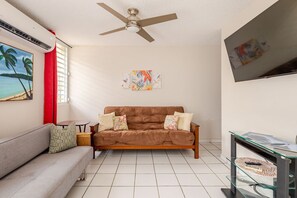 Un salon avec un canapé marron, un divan gris, un ventilateur de plafond et un téléviseur fixé au mur.