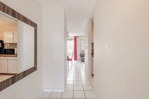 Un pasillo con una zona de cocina a la izquierda, un comedor con una silla roja y una puerta blanca al final.